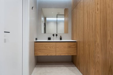 Banyo gri ve beyaz zemin ile modern bir tarzda. Aydınlık lambaları, Masa üstü ahşap çekmece ve lavabo, banyo duş ve cam bölme, havlu askısı ile bir askı ile büyük bir ayna.
