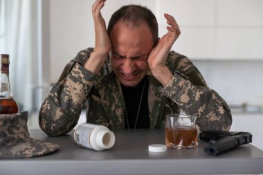 Kamuflajlı bir adam ordudan döndükten sonra depresyona girer. Alkol ve uyuşturucu hapları kullanıyor. Ağır anılar yüzünden acı çekiyor. Masanın üzerinde bir silah var. Yüksek kalite fotoğraf