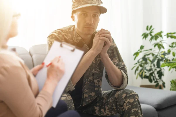 sad soldier with ptsd talking at psychiatrist and gesturing while sitting on couch during therapy session.