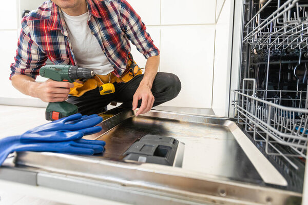 Service man repairing dishwasher in modern kitchen. Maintenance and household assistance concept . High quality photo
