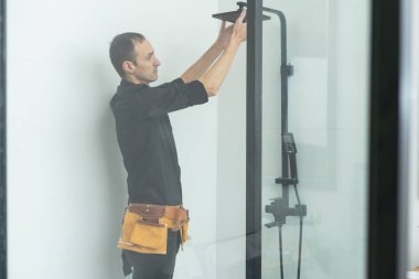 İşçi, duşun cam duvarlarını metal bir çubukla birleştiriyor.