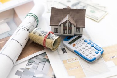 İpotek başvuru formu, hesap makinesi, planlar vs. olan bir masanın üstünde bir ev.