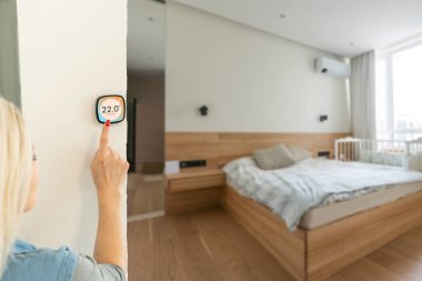 Gülümseyen Hintli kadın modern akıllı ev sistemini kullanıyor, kontrol paneli duvarda, pozitif çekici genç kadın termostatın sıcaklığını değiştiriyor ya da apartmandaki güvenlik alarmını çalıştırıyor.