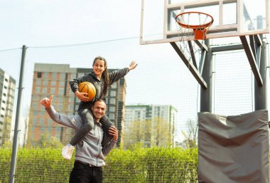 Babası, kızı omuzlarında taşıyarak basketbol topunu ağlara takmasına yardım ediyor.