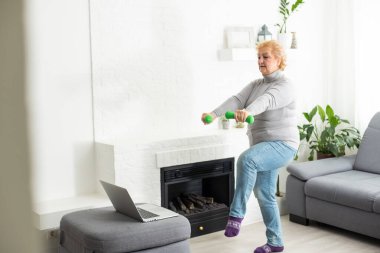 Evde antrenman. Sportif son sınıf öğrencisi laptopta ders izlerken yoga tahtası yapıyor oturma odasında egzersiz yapıyor, boş yer, panorama..