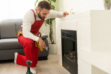 Professional technician sealing electric fireplace near white wall in room.