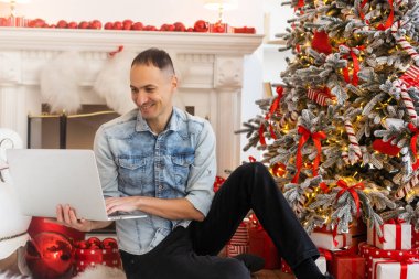 Serbest çalışan genç bir adam internet üzerinden ev ofisteki kediyle bilgisayardan video görüşmesi yapıyor. Noel havası, yılbaşı süsü, Noel tatili. Tecrit