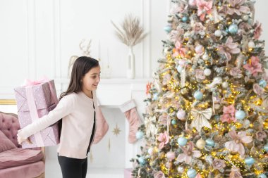 Elinde hediye tutan çok güzel bir kız. Noel havası. Çocuk mutlu bir gülümseme ile hediye verir. Mesaj için yer. Bokeh çelenkleri. Yeni Yıl.