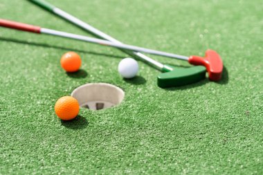 Mini-golf clubs and balls of different colors laid on artificial grass