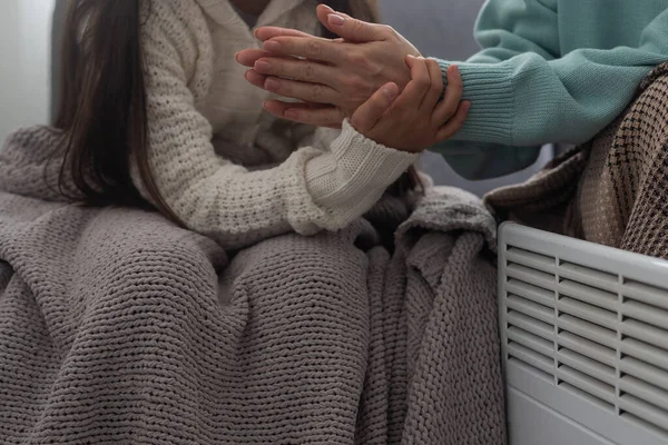 Family warming hands near electric heater at home, closeup.