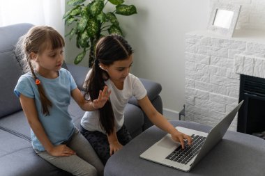 Dizüstü bilgisayarda çalışan iki kız, gülümsüyor ve ablası genç kıza yardım ediyor..