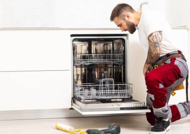 Man repairing a dishwasher with tools.