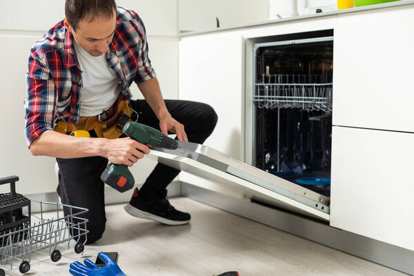 Рабочий чинит посудомоечную машину на кухне. Высокое качество фото