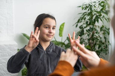 Sevimli küçük kız, anneyle ya da kadın dadıyla el hareketi öğreniyor, gülümsüyor küçük çocuk evde öğretmenle sözlü olmayan konuşma yapıyor, anaokulundan engelli çocuk özel öğretmenden ders alıyor..