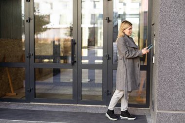 Kadın kapının yanında duruyor ve akıllı telefonuyla çevrimiçi uygulamayla kilitliyor..
