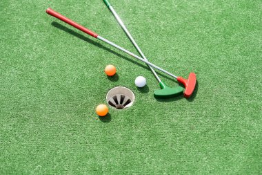 Mini-golf clubs and balls of different colors laid on artificial grass