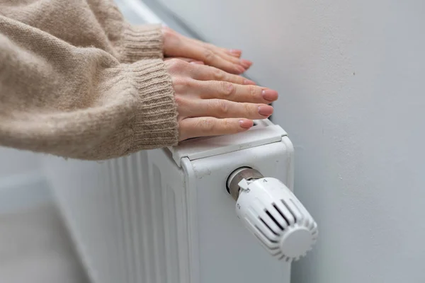 Female hands are trying to keep warm on an aluminum radiator. A woman warms herself near a radiator in winter during the energy crisis in Europe