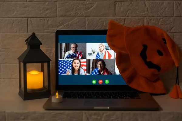 Group of people happy to see each other at virtual Halloween party. laptop computer at decorated kitchen table, waving hand and greeting friends at online video meeting.