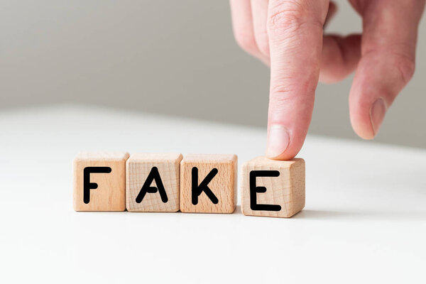 Крупный план бизнесвумен держит кубики со словом FAKE. Высокое качество фото