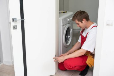 Ön ahşap giriş kapısına bir kilit takıldı. Kapı tokmağı monte eden mavi üniformalı genç çilingir işçisinin portresi. Profesyonel tamir servisi. Bakım Kavramı.