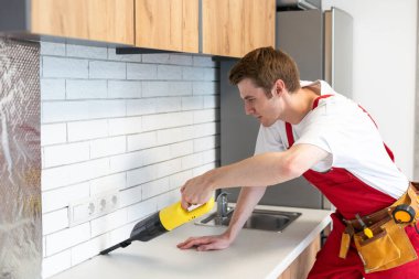 Genç neşeli adam mutfağı temizliyor. Kirli ev işleri. Evin içine toz püskürtüyor..