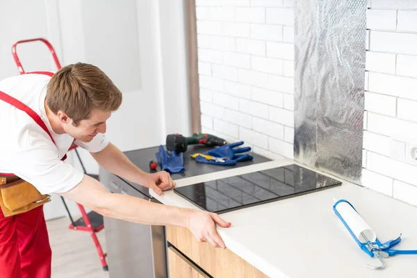 stock image craftsman installs hob in kitchen. Household Appliance Installation Services Concept.