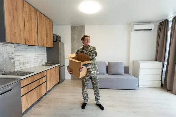 Patriotic military man in uniform keeps box in new apartments. Buying a property.
