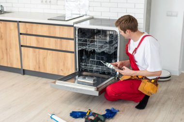 Üniformalı teknisyen ya da işçi mutfak mobilyalarına bulaşık makinesi yerleştiriyor. Tamirci bulaşık makinesini tamir ederken işçi kıyafeti giyer. Koruyucu eldivenlerde uzman Bulaşık makinesini tamir eder.