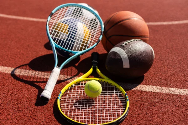 A variety of sports equipment including an american football, a soccer ball, a tennis racket, a tennis ball, and a basketball.