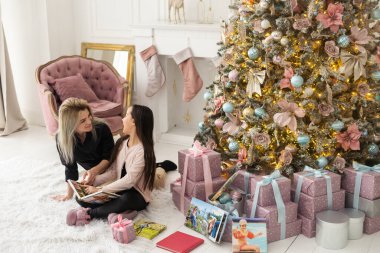 Uzun saçlı güzel genç anne küçük kızıyla birlikte bir fotoğraf kitabı okuyor. Noel için ev dekorasyonu. sıcak renkli fotoğraf
