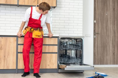 Üniformalı teknisyen ya da işçi mutfak mobilyalarına bulaşık makinesi yerleştiriyor. Tamirci bulaşık makinesini tamir ederken işçi kıyafeti giyer. Koruyucu eldivenlerde uzman Bulaşık makinesini tamir eder.