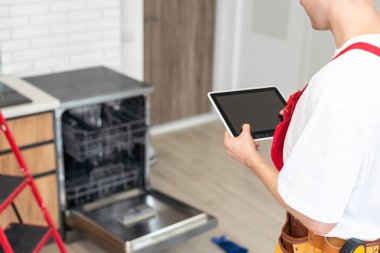 Genç erkek teknisyen mutfakta bulaşık makinesi dijital multimetre ile kontrol.