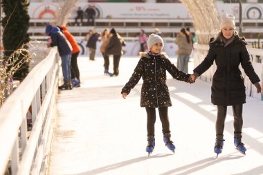 Mother with her daughters skates on ice skating.