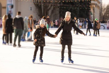 Mother with her daughters skates on ice skating.