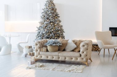 Yeni yıl ağacının süslendiği klasik bir beyaz noel iç mimarisi. Gri sandalye ve hediyeler ağacın altında.