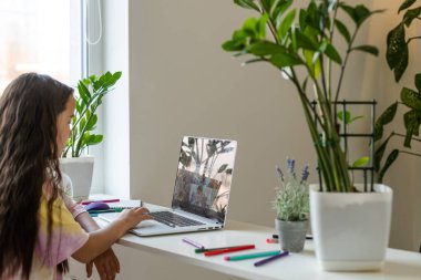 Online eğitim. Öğretmen çocuğa sohbet sınıfı görüntülü konuşma videosu konferansı öğretiyor. Küçük kız evde bir masada oturan bir dizüstü bilgisayarla ders veriyor..