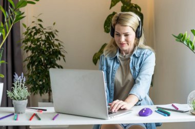 Laptop ekranına bakıp gülümseyen genç bir kadın, mesajda iyi haberler okuyor, video izliyor, sosyal ağda sohbet ediyor ya da evde online alışveriş yapıyor, bilgisayarla boş vakitlerin keyfini çıkarıyor.