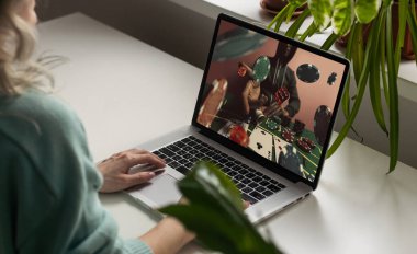 İnternetteki kumarhane. Genç bir kadın online bir oyunda bahis oynar. Kadının önündeki masada bir dizüstü bilgisayar var, çipler. Kartlar. Kumar, hobi, riskli aktiviteler. Gri-yeşil arka plan. Yüksek kalite fotoğraf