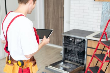 Üniformalı teknisyen ya da işçi mutfak mobilyalarına bulaşık makinesi yerleştiriyor. Tamirci bulaşık makinesini tamir ederken işçi kıyafeti giyer. Koruyucu eldivenlerde uzman Bulaşık makinesini tamir eder.