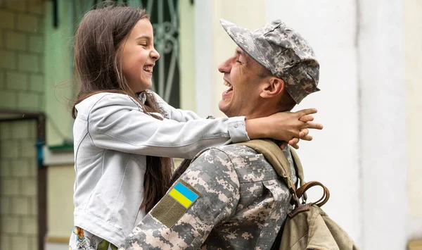 Soldier in Ukrainian military uniform hugging his daughter. Family reunion.