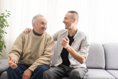 Young adult caucasian son listening and supporting his old elderly senior father at home indoors. Care and love concept