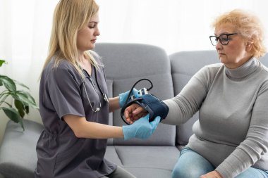 Bakıcı genç hemşire engelli ya da yaralı yaşlı kadının el ele tutuşmasına yardım ediyor. Sağlık sorunu olan yaşlı bir kadın engelli ve hastanede yürüyen bir kadın ile evde oturuyor.
