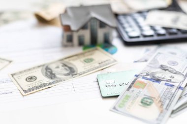 Gelir vergisi formları veya bütçe planlaması üzerinde çalışan muhasebeci döviz notları, hesap makinesi ve 3d ev modeli ile birlikte.