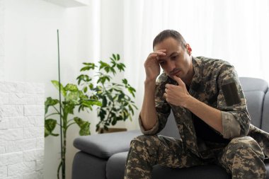 Askeri üniformalı bir adam pencerenin yanındaki sandalyede oturuyor. Konsept: Psikolog randevusunda bir asker, travma sonrası stres sendromu, zihinsel bozukluk, savaşın sonuçları..