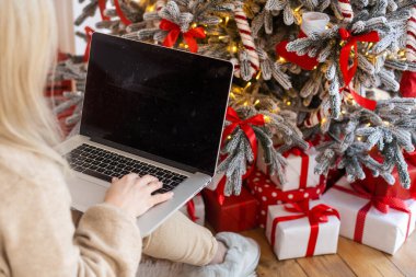 Noel ağacı önünde dizüstü bilgisayarda çalışan mutlu genç kadın