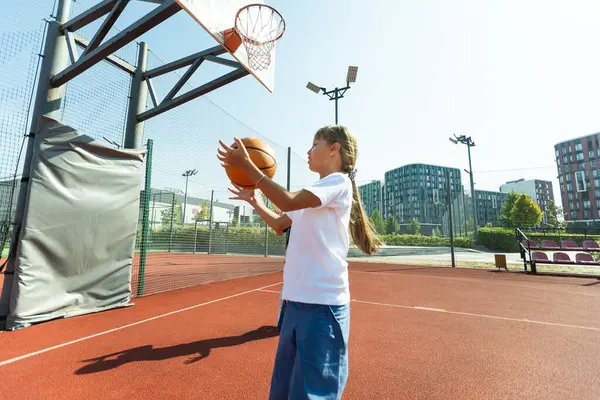 Concept of sports, hobbies and healthy lifestyle. Young athletic girl is training to play basketball on modern outdoor basketball court. Happy woman. High quality photo