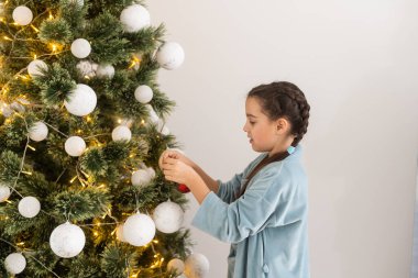 Küçük kız içeride Noel ağacını süslüyor. Noel 'den önceki sabah.