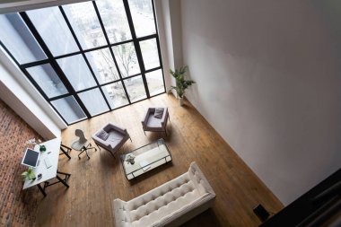 Modern minimalist tasarımı olan parlak bir oda. Duvarda bir kanepe ve çiçekler, duvarda tablolar var. Yan panoramik pencere.