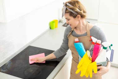 Ev işleri yapan genç bir kadın. Elinde temizlik aletleri olan kadın. Plastik koruyucu sarı eldivenler giyen, elinde bez parçası ve sprey deterjan tutan bir kadın. Bahar temizliği için asla geç değildir..