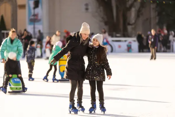 Mother with her daughters skates on ice skating.